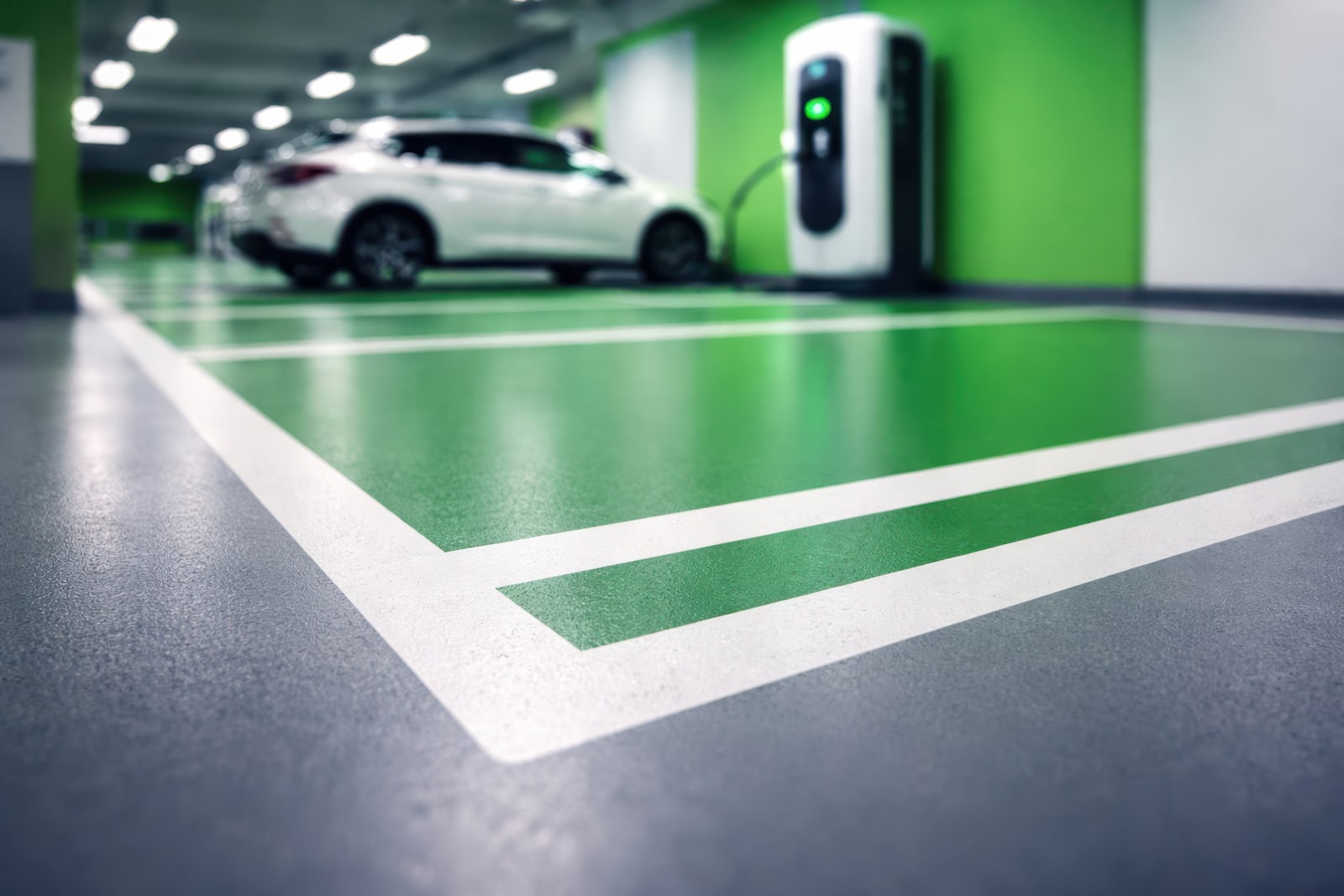 Green EV charging bay with white line markings beside a grey car park traffic lane